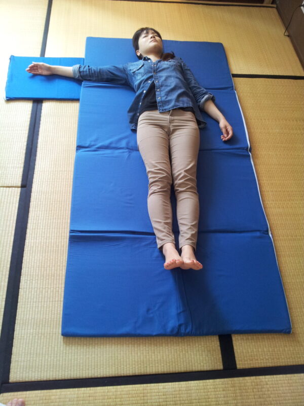 Femme allongée sur un tatami portable bleu déplié au sol – surface de shiatsu légère et compacte tatamiportable.com