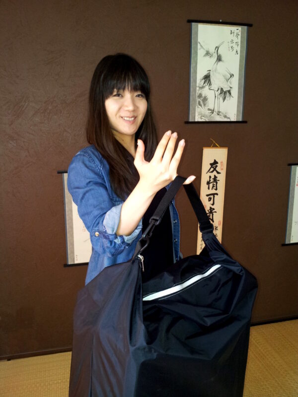 Femme souriante tenant le sac de transport d'un tatami portable léger et compact – tatamiportable.com